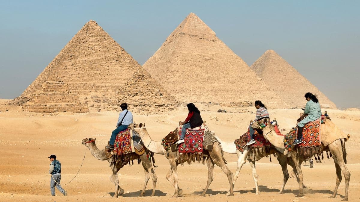 Four people on camels near pyarmids